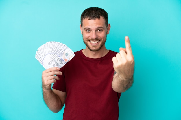 Joven brasileño tomando un montón de dinero sobre antecedentes aislados haciendo gesto de venida