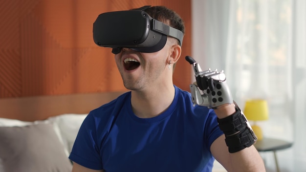Joven brazo biónico contemporáneo usa auriculares de realidad virtual jugando videojuegos sentado en la cama