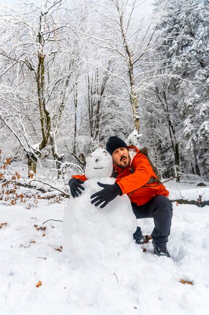 Un joven bromeando con un muñeco de nieve en el bosque nevado del parque natural de Artikutza en oiartzun cerca de San Sebastián, Gipuzkoa, País Vasco. España