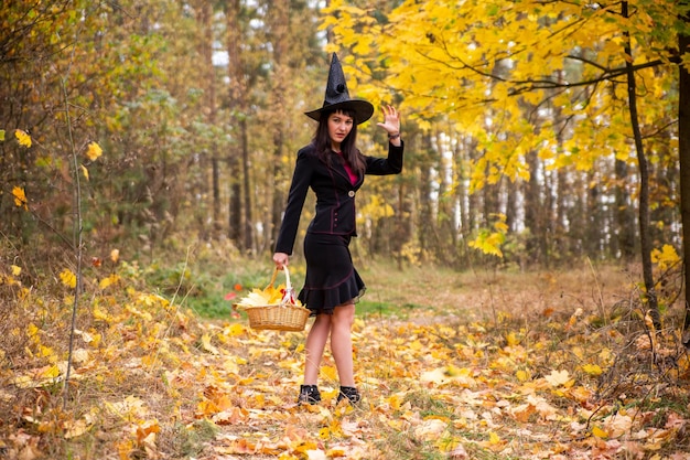 Joven bruja atractiva camina en el bosque de otoño naranja.Concepto de Halloween.