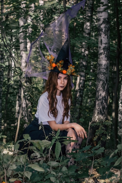 Joven bruja bonita con sombrero negro de cerca en el bosque. Whitch cosplay de halloween. Procesamiento de arte.