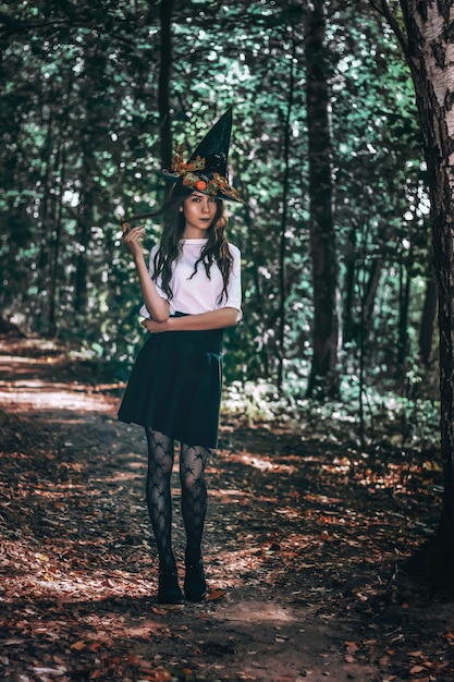 Joven bruja bonita con sombrero negro de cerca en el bosque. Whitch cosplay de halloween. Procesamiento de arte.