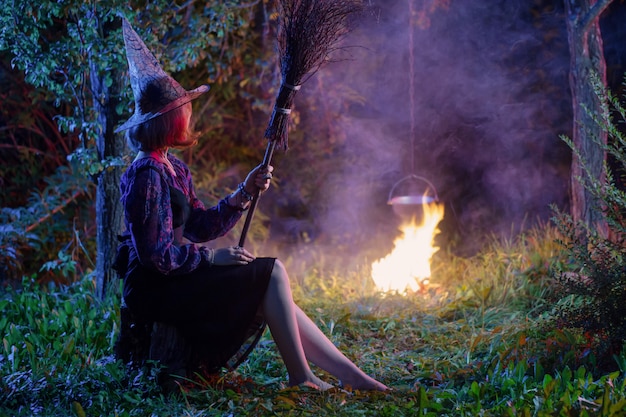 Joven bruja por fuego en bosque nocturno