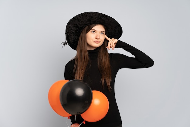 Joven bruja sosteniendo globos aerostáticos negros y naranjas