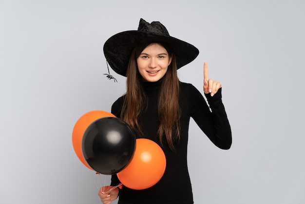 Joven bruja sosteniendo globos aerostáticos negros y naranjas