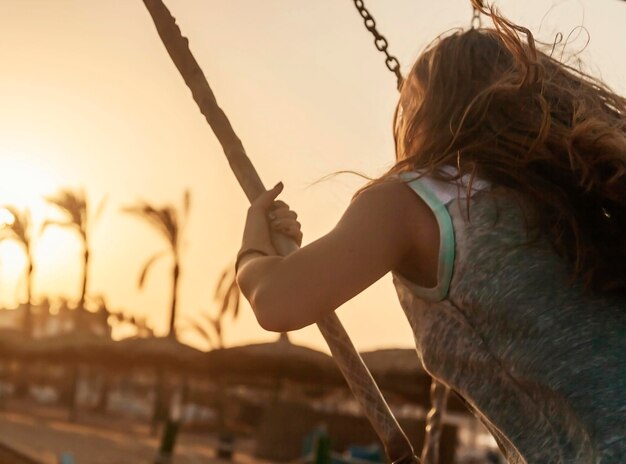 Foto joven cabalgando sobre un columpio al atardecer sobre un fondo de palmeras