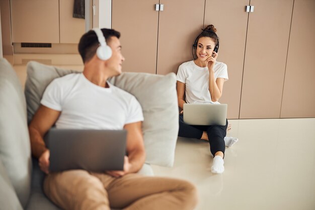 Joven caballero en headphoens y novia trabajando desde casa