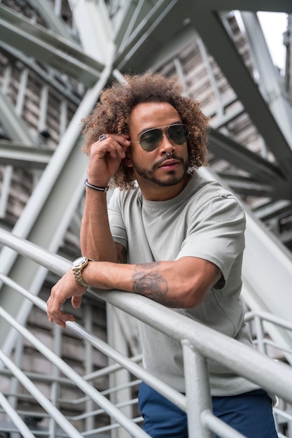 Joven con cabello afro con gafas de sol en las escaleras de la ciudad, moda urbana, concepto genial de un tipo hipster con estilo