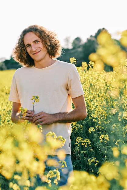 Joven con cabello rizado con una flor amarilla en un campo de flores de colza