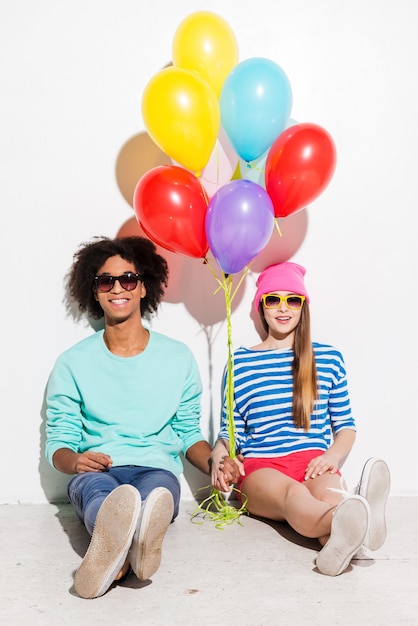 Joven cadera y enamorada. Funky pareja joven sosteniendo globos mientras está sentado contra el fondo blanco.