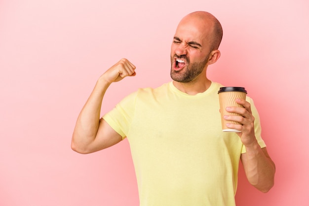 Joven calvo caucásico sosteniendo un café para llevar aislado sobre fondo rosa levantando el puño después de una victoria, concepto ganador.