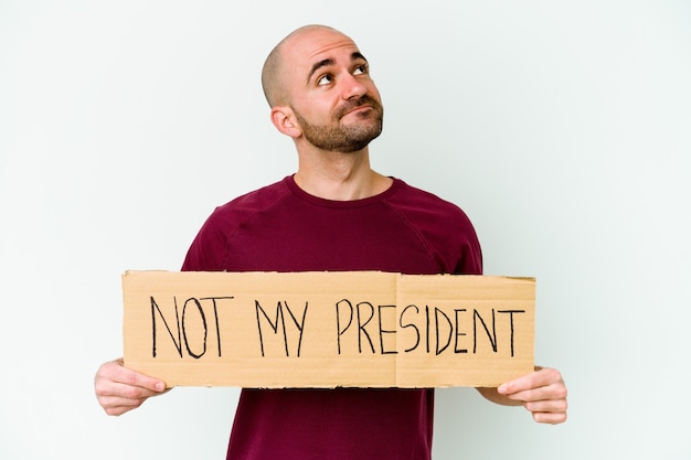 Foto joven calvo caucásico sosteniendo un cartel de no es mi presidente aislado en la pared blanca soñando con lograr metas y propósitos