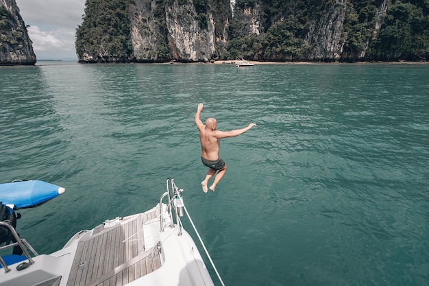 Joven calvo saltando de yate en el mar azul. Phuket. Tailandia Viaje a un destino cálido