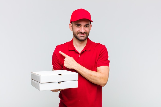 Joven calvo sonriendo alegremente, sintiéndose feliz y apuntando hacia un lado y hacia arriba, mostrando el objeto en el espacio de la copia