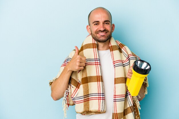 Joven calvo sosteniendo linterna vintage aislado sobre fondo azul sonriendo y levantando el pulgar hacia arriba