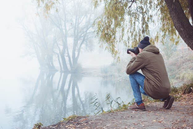 Un joven con una cámara toma fotos de la naturaleza otoñal mientras viaja.