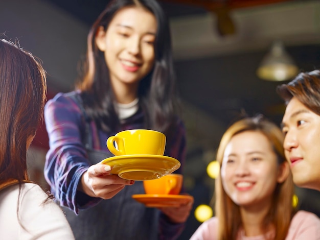 joven camarera asiática sonriente sirviendo café a los clientes