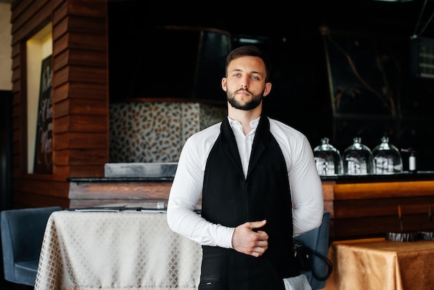 Un joven camarero con barba se pone un delantal y se prepara para un día de trabajo en un buen restaurante