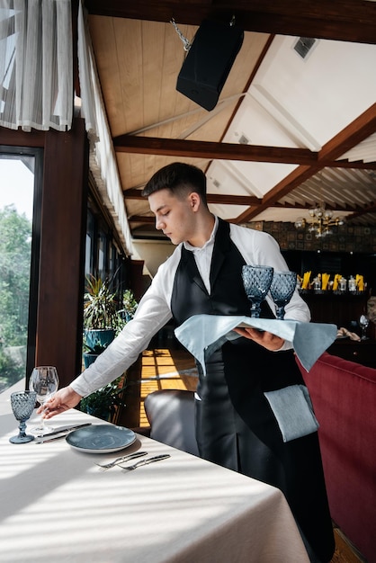 Un joven camarero con un elegante uniforme se dedica a servir la mesa en un hermoso restaurante gourmet Un restaurante de alto nivel Servicio de mesa en el restaurante