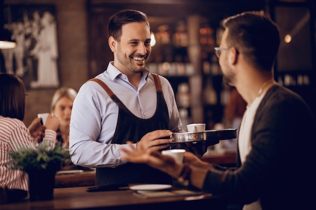 Joven camarero feliz hablando con su cliente mientras le sirve café en un pub