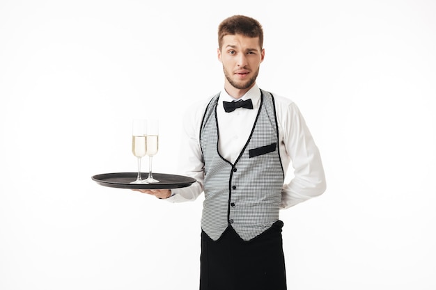 Foto joven camarero en uniforme sosteniendo la bandeja con copas de champán mientras pensativamente