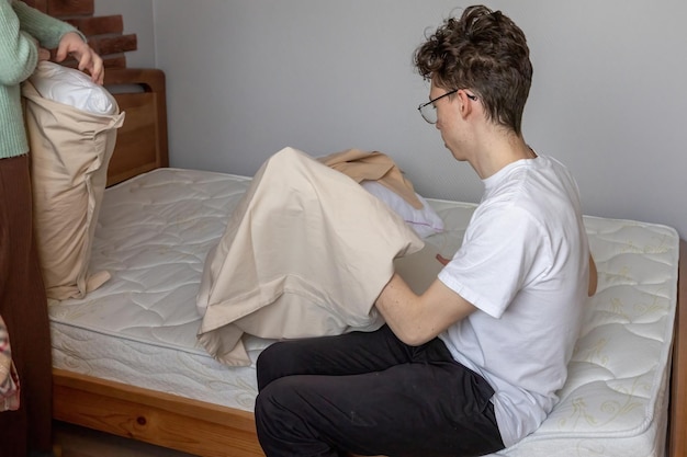 Un joven cambia la ropa de cama en la cama.