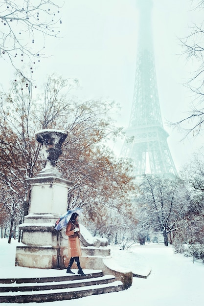 Una joven camina en un invierno nevado en París contra la Torre Eiffel
