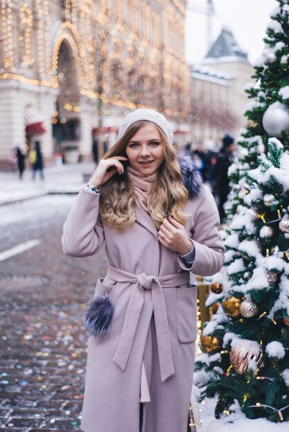 Una joven camina en Navidad en la plaza cerca de los árboles de Navidad decorados. Candy es una piruleta en forma de corazón.