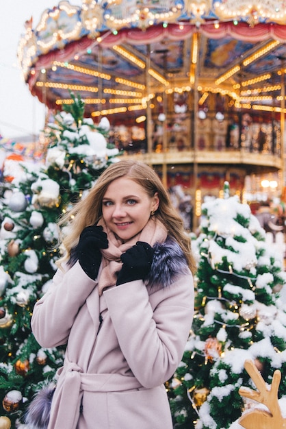 Una joven camina en Navidad en la plaza cerca de los árboles de Navidad decorados. Candy es una piruleta en forma de corazón.