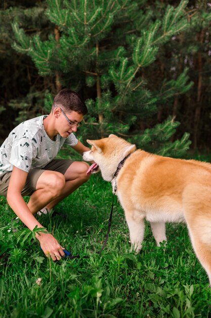 Un joven camina en un parque de verano con un joven cachorro de raza akita.