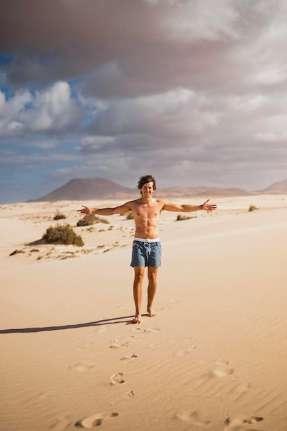 Foto joven caminando feliz y sin camisa en la arena del desierto de las dunas de fuerteventura en verano