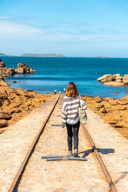 Foto una joven en el camino para descender los barcos junto al faro mean ruz, puerto de ploumanach, en la localidad de perros-guirec, cotes-d'armor, en la bretaña francesa, francia.