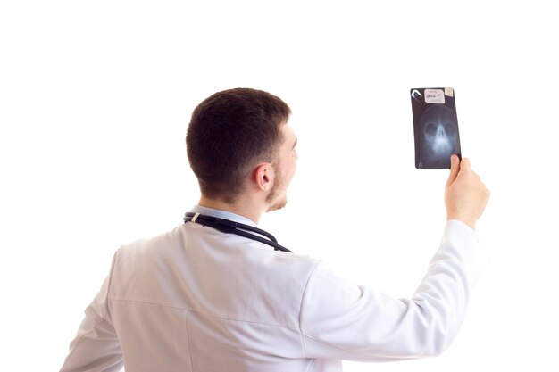 Joven con camisa azul, corbata y bata de doctor con estetoscopio en el cuello sosteniendo Xray