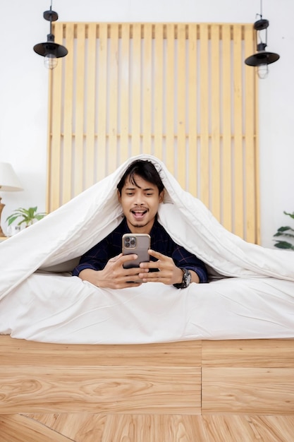joven con camisa azul jugando al celular en la cama