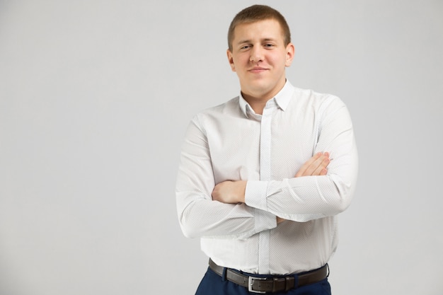 Joven en camisa blanca se encuentra aislado sobre fondo blanco con los brazos cruzados sobre el pecho