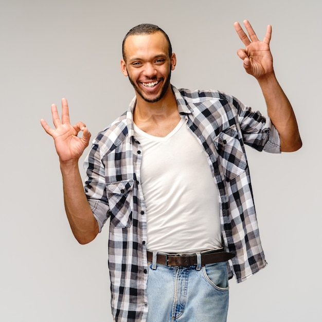 joven con camisa casual y mostrando el signo de ok sobre gris claro.