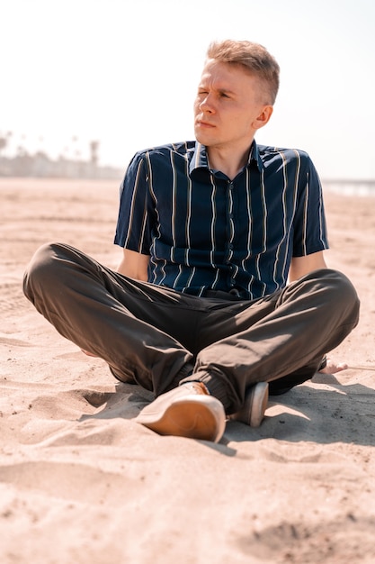 Un joven en camisa descansa sobre la arena de una playa en Los Ángeles el concepto de unas vacaciones de verano