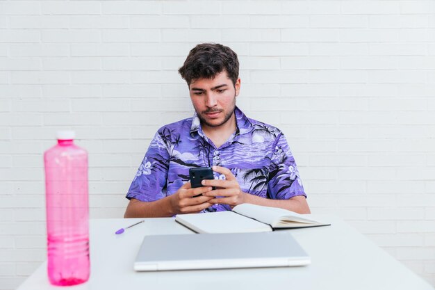 Joven con camisa hawaiana azul mirando un teléfono inteligente con fondo de ladrillo blanco concepto criptomoneda de teletrabajo