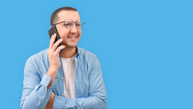 Joven en una camisa de mezclilla hablando por un teléfono móvil sobre un fondo blanco.