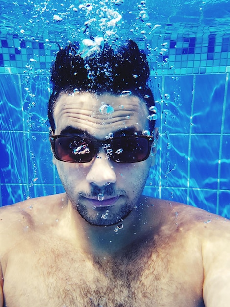 Joven sin camisa nadando en la piscina