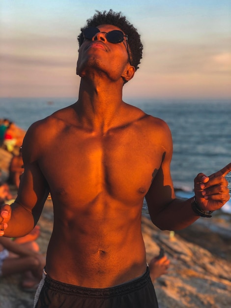 Foto un joven sin camisa de pie en la playa durante la puesta de sol