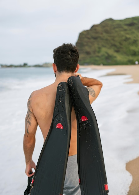 Joven sin camisa en la playa con equipo de buceo