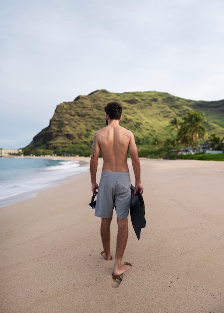 Joven sin camisa en la playa con equipo de buceo