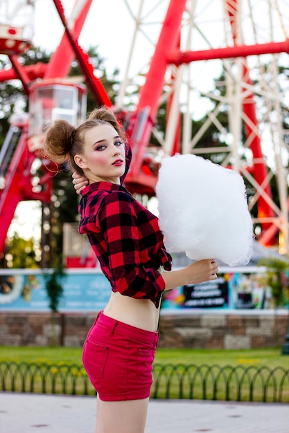 Una joven con una camisa roja con algodón de azúcar mira hacia el cielo en el parque