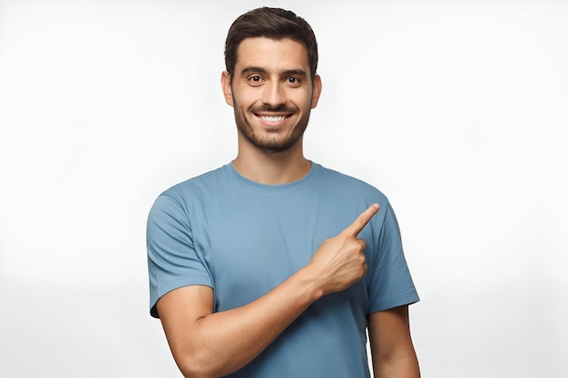 Joven en camiseta azul apuntando a la derecha con su dedo aislado en un fondo gris