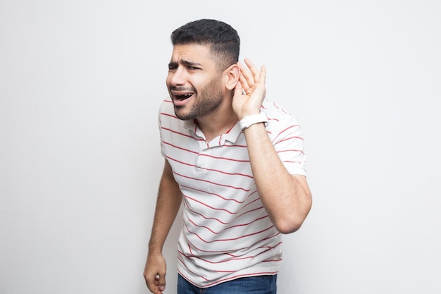 Foto joven con camiseta a rayas de pie con la mano en la oreja y quiere escuchar algo