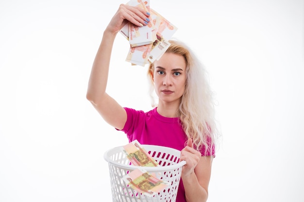 Una joven con una camiseta rosa tira billetes rusos a la basura con un fondo blanco El concepto de una economía en caída