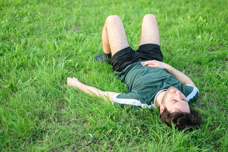 Joven con camiseta verde tumbado en el césped en el parque después de hacer ejercicio agotado