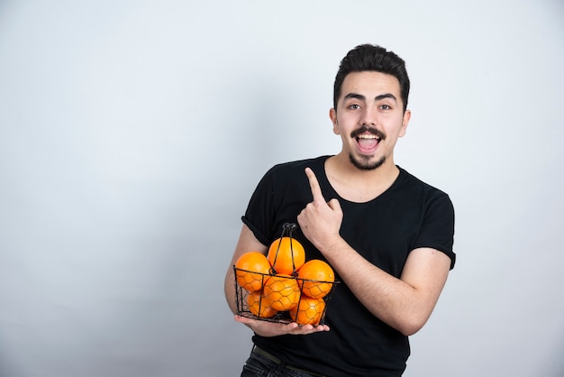 joven con canasta metálica llena de frutas naranjas apuntando hacia arriba.