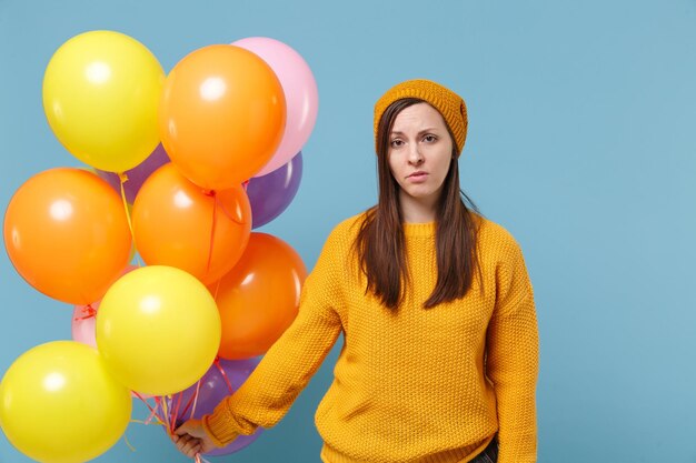 Una joven cansada disgustada con un sombrero de suéter posando aislada en un fondo azul en el estudio. Concepto de emoción de la gente de la fiesta de cumpleaños. Simulacros de espacio de copia. Celebrando sostener un globo de aire colorido.